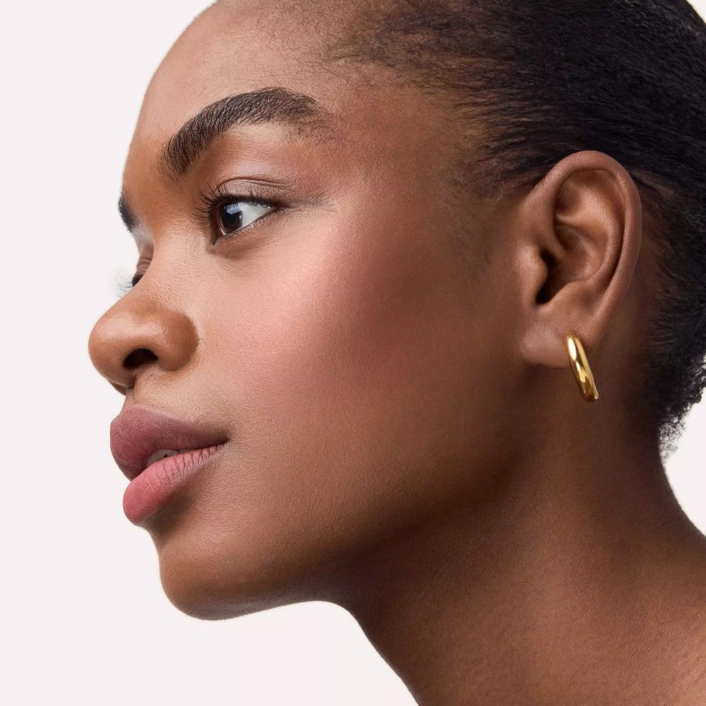 Nahaufnahme einer Frau mit gebräunter Haut und Rouge auf den Wangen. Sie trägt goldene Creolen.