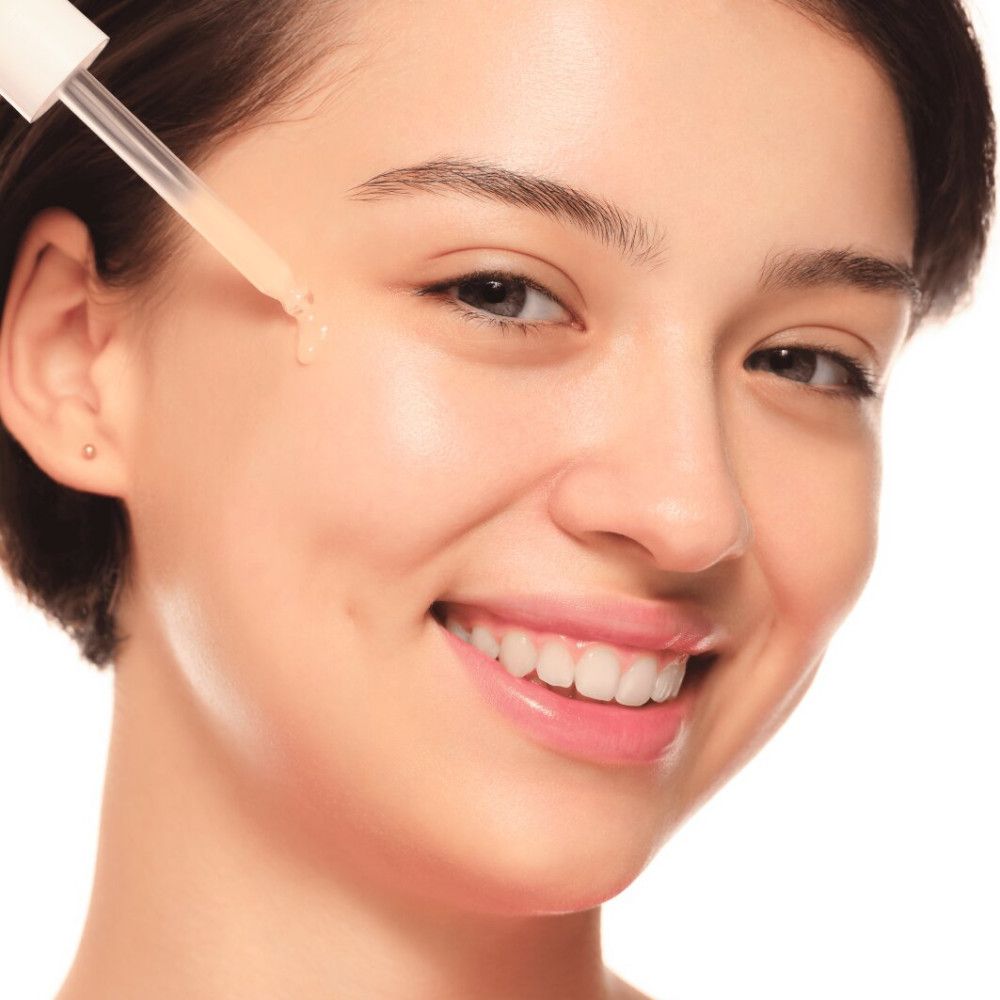 Frau mit Serum auf der Haut. Weißer Hintergrund. Tropfer in der Nähe des Gesichts.