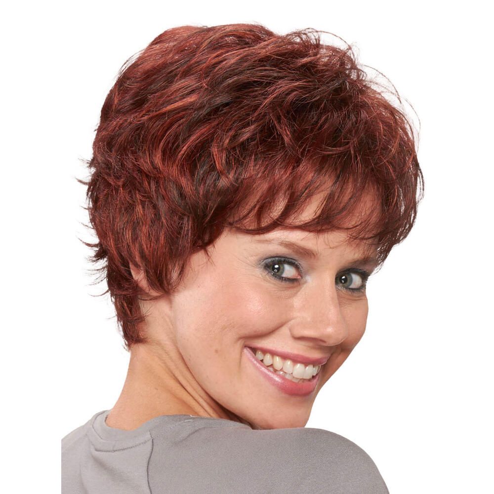 Kurzhaarperücke in Rotbraun. Frau lächelt. Blick nach vorn. Lockige Struktur. Pony. Graues Oberteil.