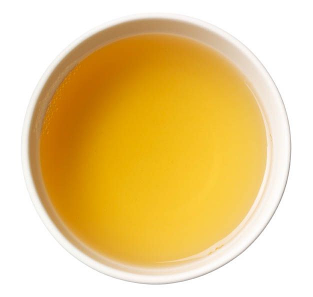 Weisse Tasse mit gelbem Tee, Draufsicht. Der Tee ist klar und von goldener Farbe.