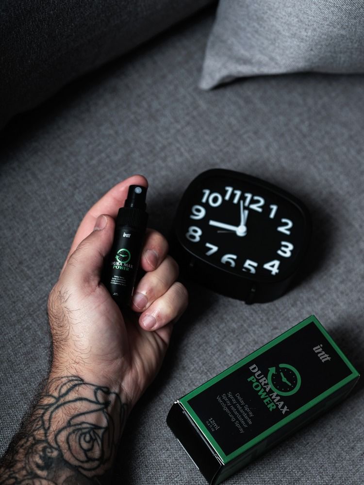 Hand hält Sprühflasche und Verpackung. Schwarze Flasche und Verpackung mit "Dura Max Power"-Logo.