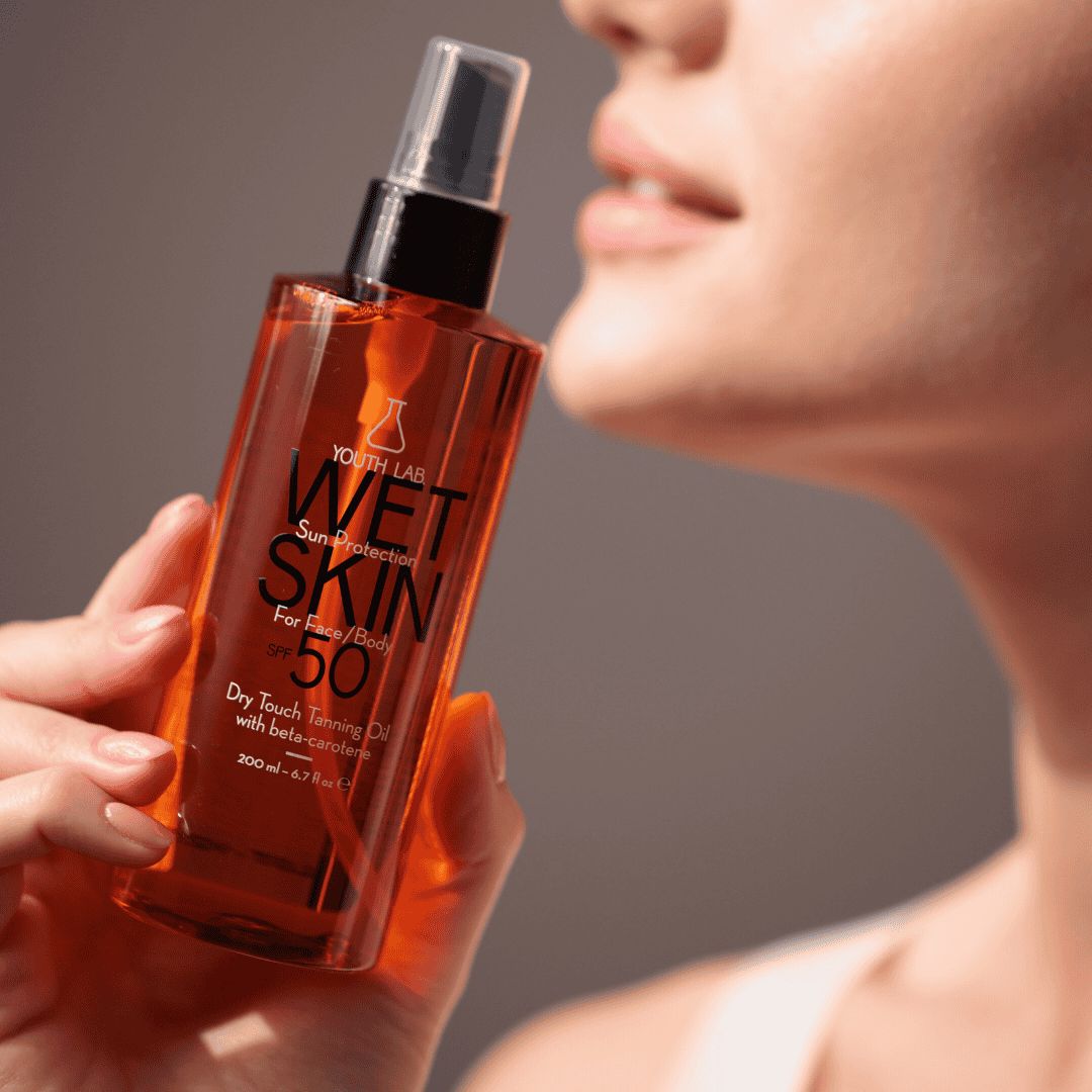 Eine Frau hält eine orangefarbene Flasche. Aufschrift: YOUTH LAB WET SKIN SPF 50. Schwarzer Sprühkopf.