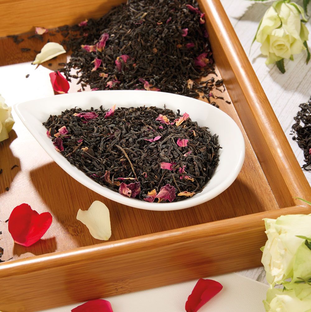 Schwarzer Tee China Rose in einer weißen Schale auf einem Holztablett. Rosenblätter als Dekoration.