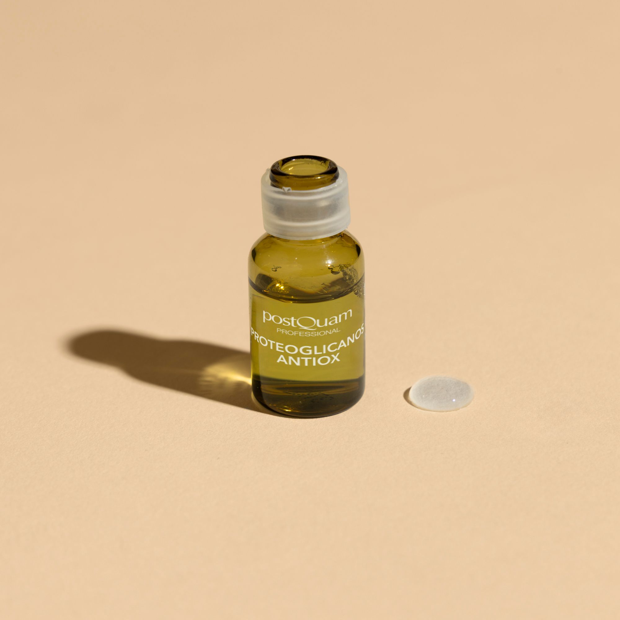 Eine einzelne Postquam Proteoglykane Antioxidant Ampulle mit Verschlusskappe und eine Kappe daneben. Auf hellem Hintergrund.
