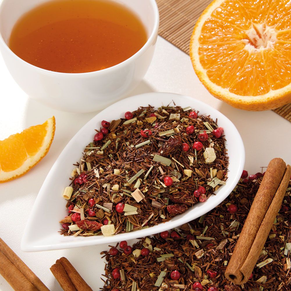 Tee mit Zutaten in weißer Schale, daneben Tasse Tee, Orangenscheibe und Zimtstangen.