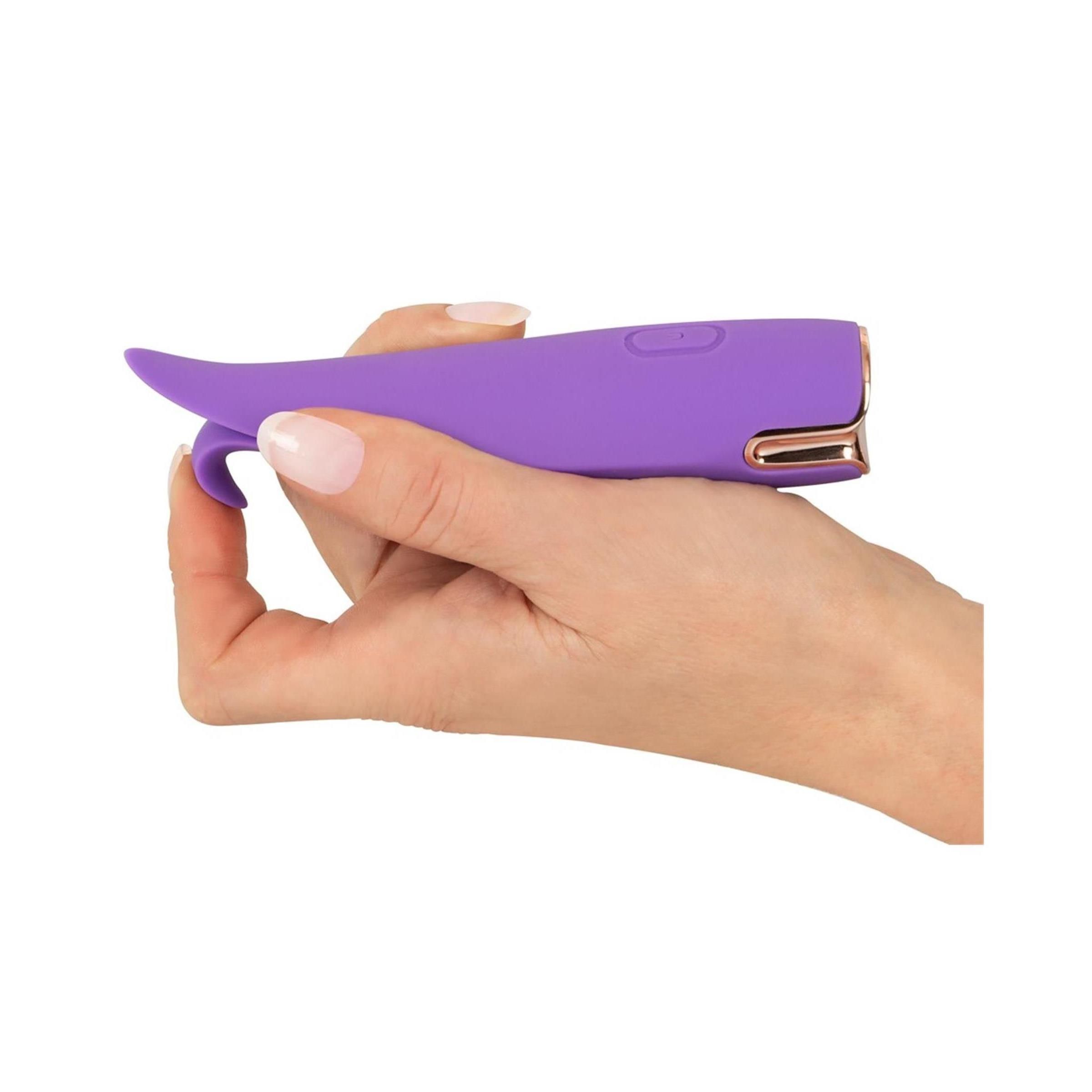 Hand hält lila Stimulator. Goldfarbene Akzente. Ein Knopf. Form mit zwei Blütenblättern.