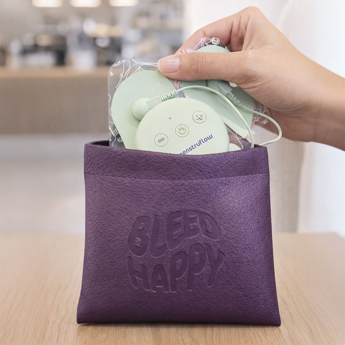 Hand hält ein grünes EMS-Gerät mit Pads und Kabeln aus einer lila Tasche.