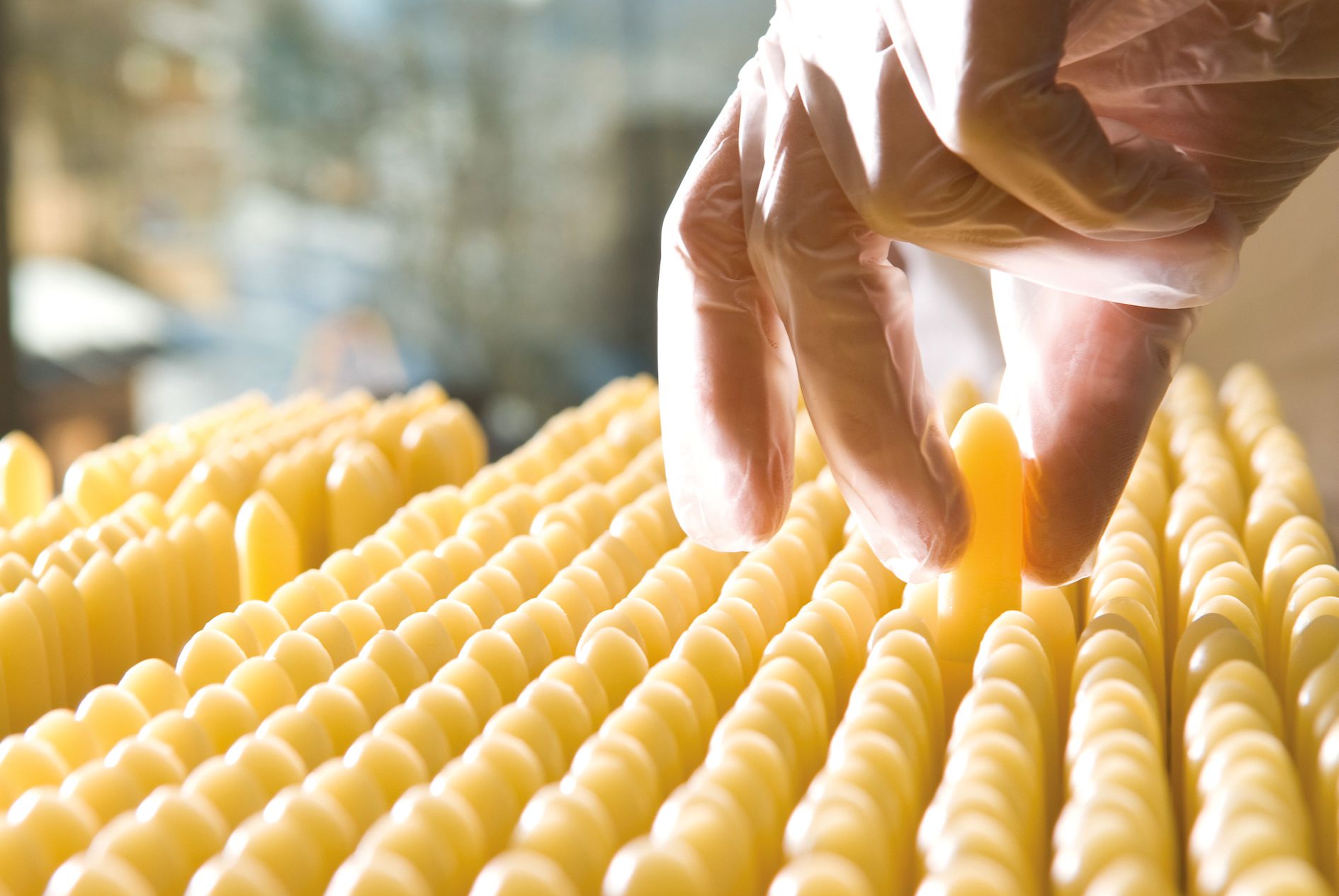 Reihenweise gelbliche Stifte, eine Hand mit Handschuh greift einen Stift.