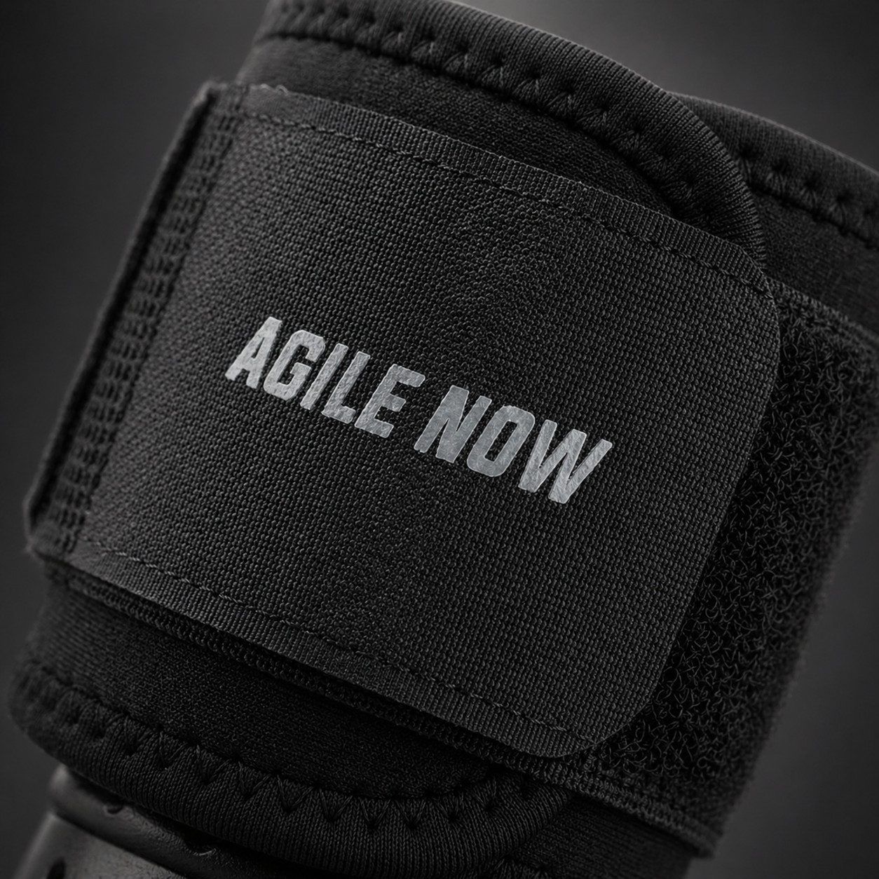 Schwarze Handgelenkbandage mit Klettverschluss und dem Aufdruck "AGILE NOW".