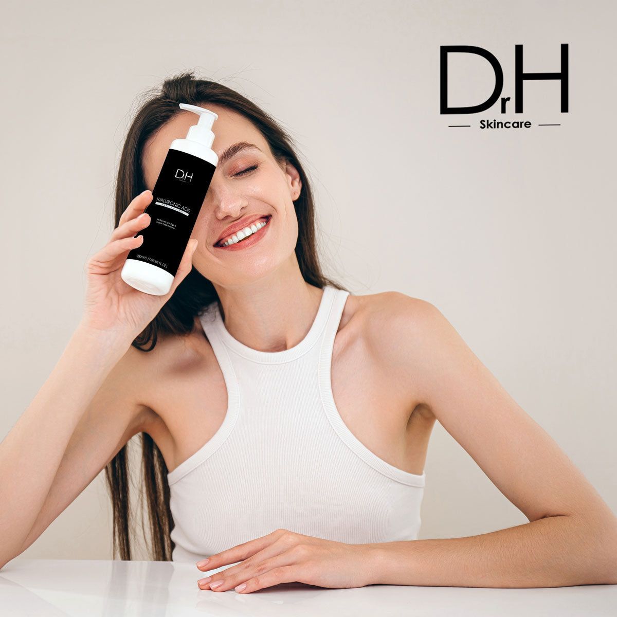Frau hält Flasche vor dem Gesicht. Schwarzes Etikett. Aufschrift: HYALURONIC ACID, Anti-Aging. Mit Dosierpumpe. Logo: D.H. Skincare.