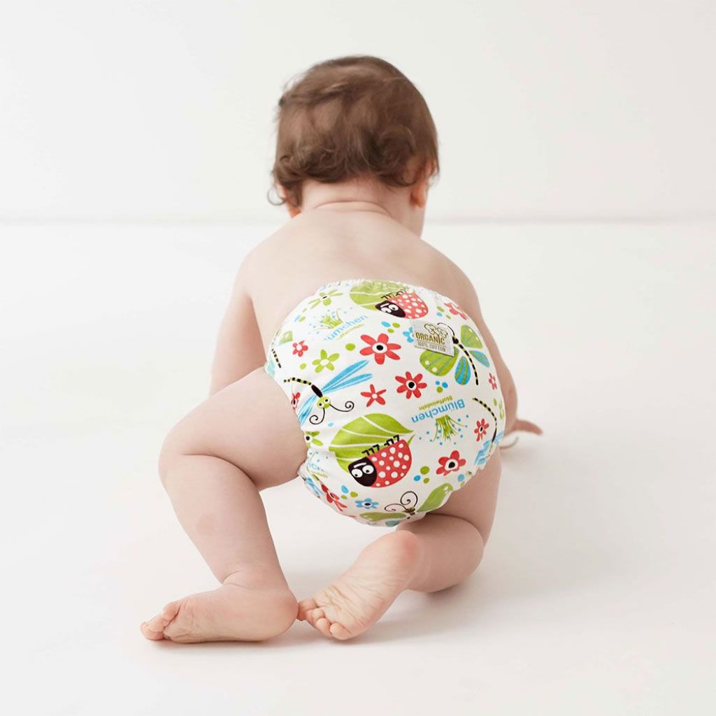 Baby krabbelt auf weißem Hintergrund. Stoffwindel mit Blumen- und Insektenmuster. Weiße Druckknöpfe. Label mit Logo. Mehrfarbiges Design.