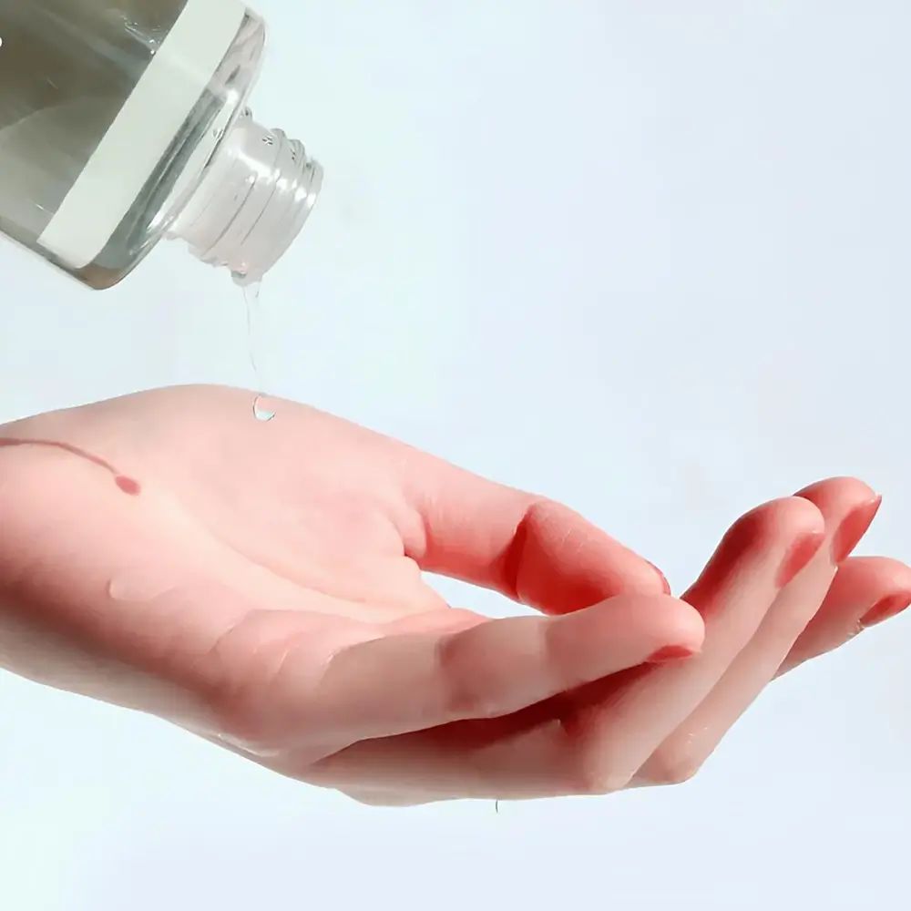 Hand mit rotem Nagellack, die Flüssigkeit aus einer Flasche empfängt. Flüssigkeit tropft auf die Handfläche.