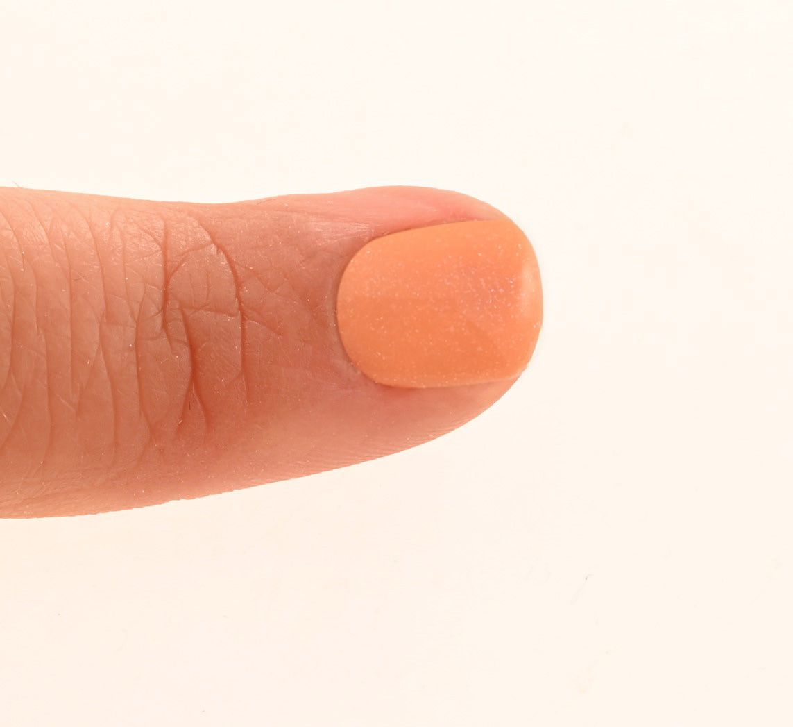 Finger mit lackiertem Nagel. Der Nagel ist mit einem orangefarbenen Nagellack bedeckt.