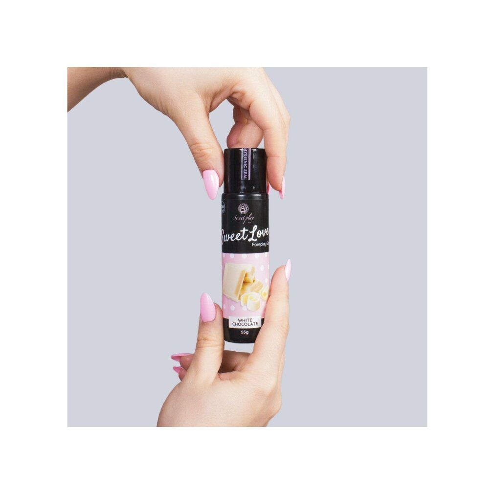 Hände halten eine schwarze Flasche mit weißem Etikett. Sweet Love Foreplay Gel. Rosa lackierte Fingernägel.