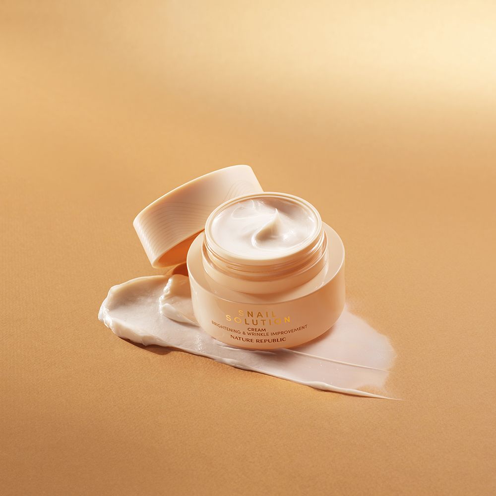 Geöffnete Creme-Dose mit Creme-Klecks. Aufschrift: Snail Solution, Nature Republic. Beige Dose und Deckel.