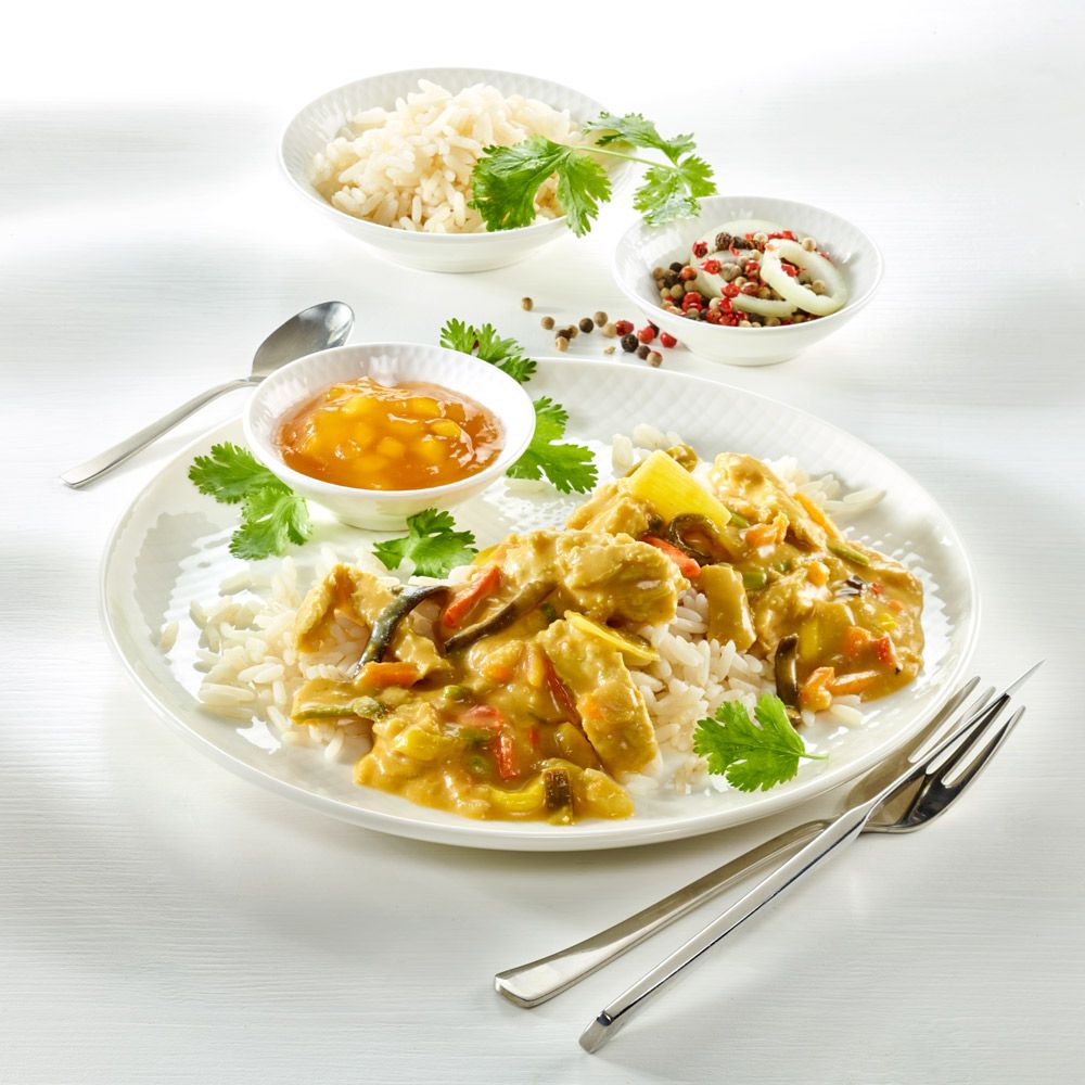 Teller mit Veggie Thai Curry auf Reis, garniert mit Koriander. Beilagen: Reis, Soße, Zwiebeln, Pfeffer.