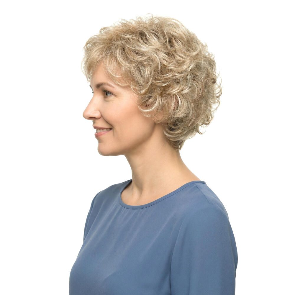 Blond gelockte Perücke. Seitenansicht einer lächelnden Frau mit blauem Oberteil. Kurze, wellige Frisur.