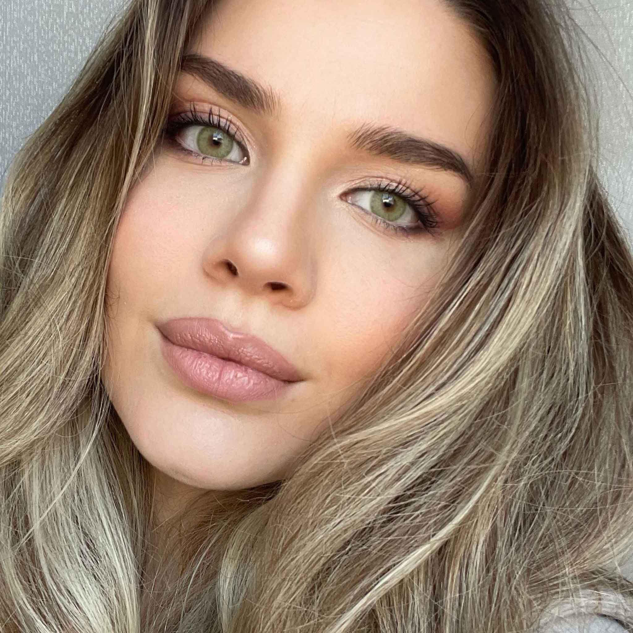 Porträt einer Frau mit grünen Augen. Die Frau hat blonde Haare und trägt Make-up. Der Blick ist direkt in die Kamera gerichtet.