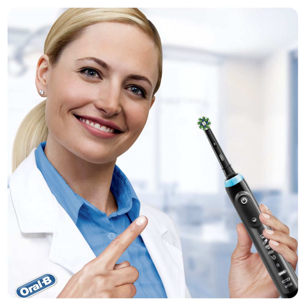 Eine Frau hält eine schwarze Oral-B Zahnbürste mit einer grünen Aufsteckbürste. Sie zeigt auf die Bürste.