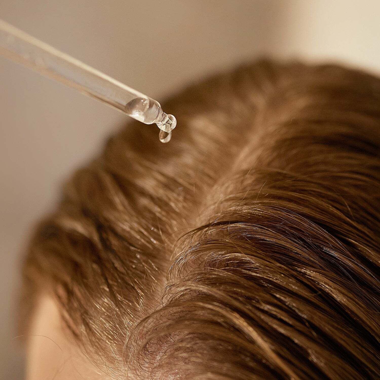 Nahaufnahme von Haaren, auf die Flüssigkeit aus einer Pipette getropft wird.