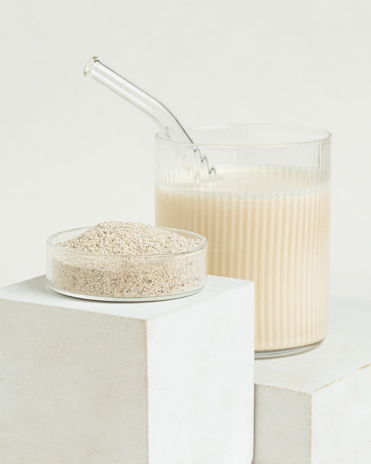 Kleiner Behälter mit Topinambur Pulver neben einem Glas Milch mit Strohhalm.