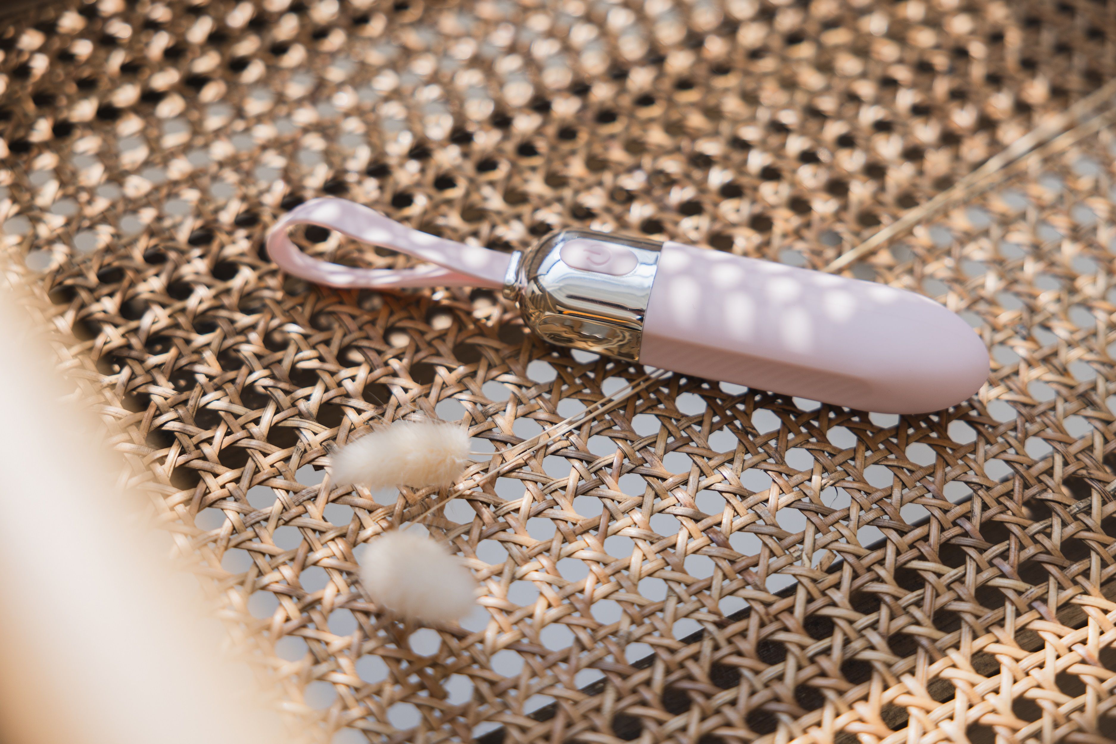 Rosa Vibrator auf einem Stuhl. Silberfarbener Kopf, Schlaufe. Zwei Wattepads daneben.