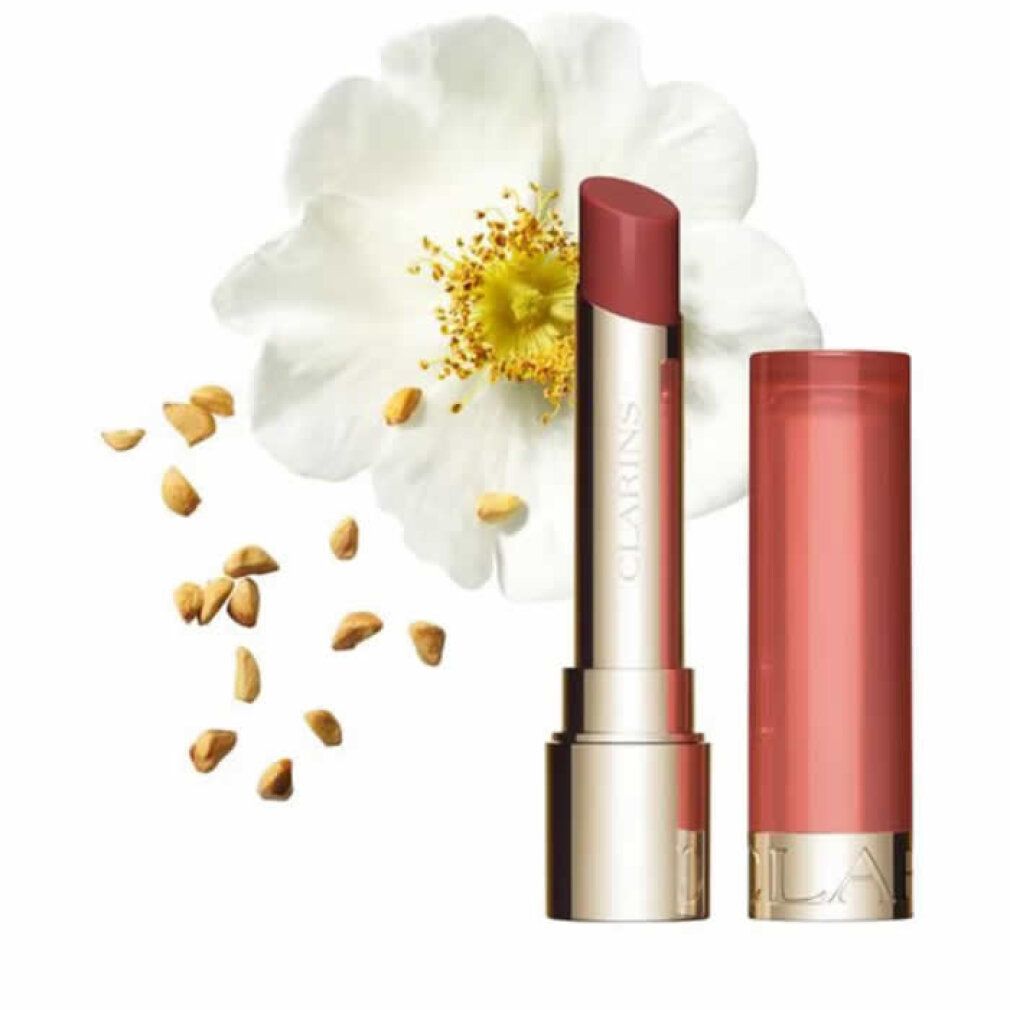 Lippenbalsam neben Blüte und Samen. Goldfarbener Behälter mit rosafarbenem Lippenstift. Marke Clarins sichtbar.