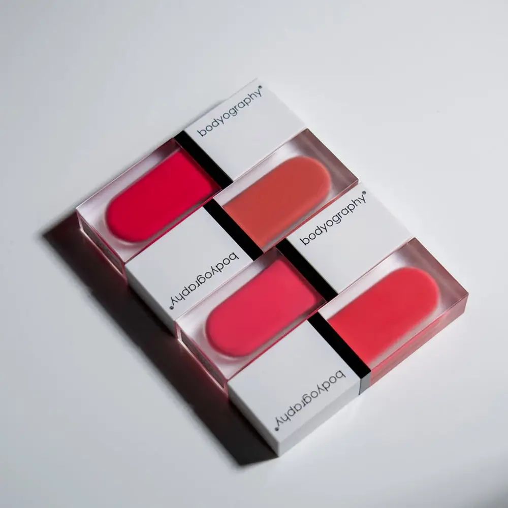 Mehrere Flüssigrouge-Verpackungen. Rosa Farbtöne. Marke BODYOGRAPHY. Transparente Behälter mit weißen Deckeln.