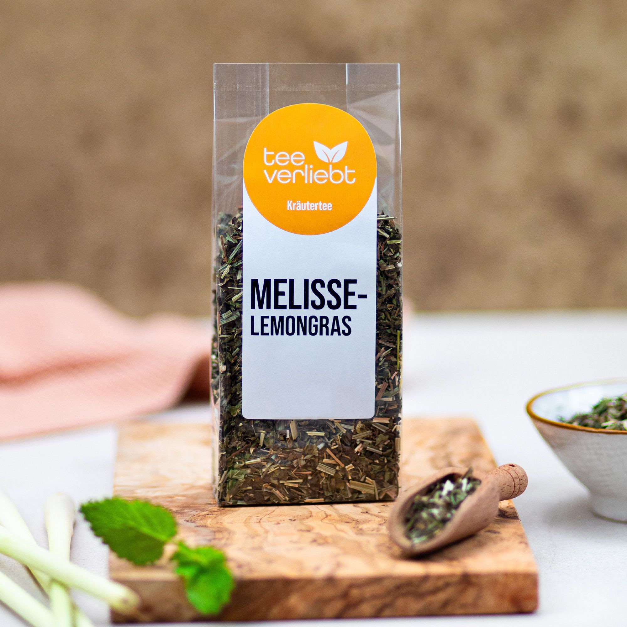 Klarsichtbeutel mit Kräutertee auf Holzbrett. "tee verliebt" und "Melisse-Lemongras" auf Etikett.