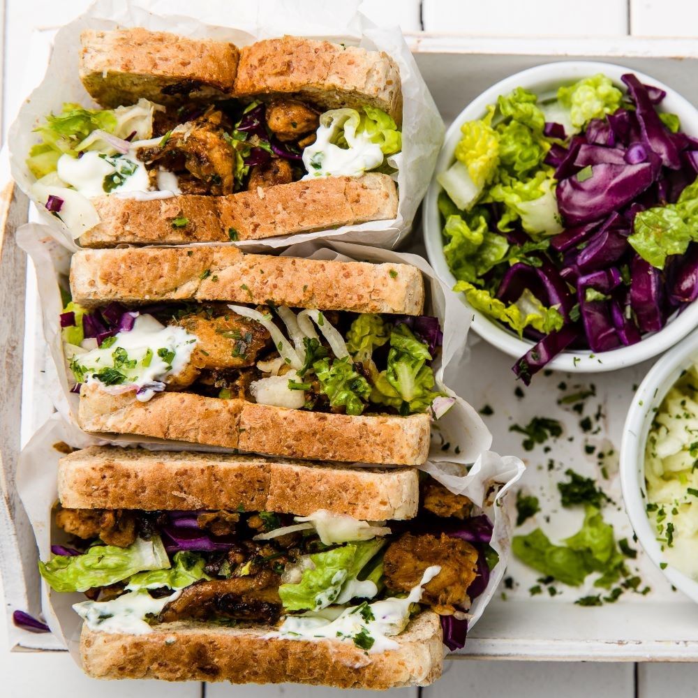 Sandwiches auf Tablett. Mehrere Schichten mit Fleisch, Gemüse und Sauce. Salat und Krautsalat in Schalen.