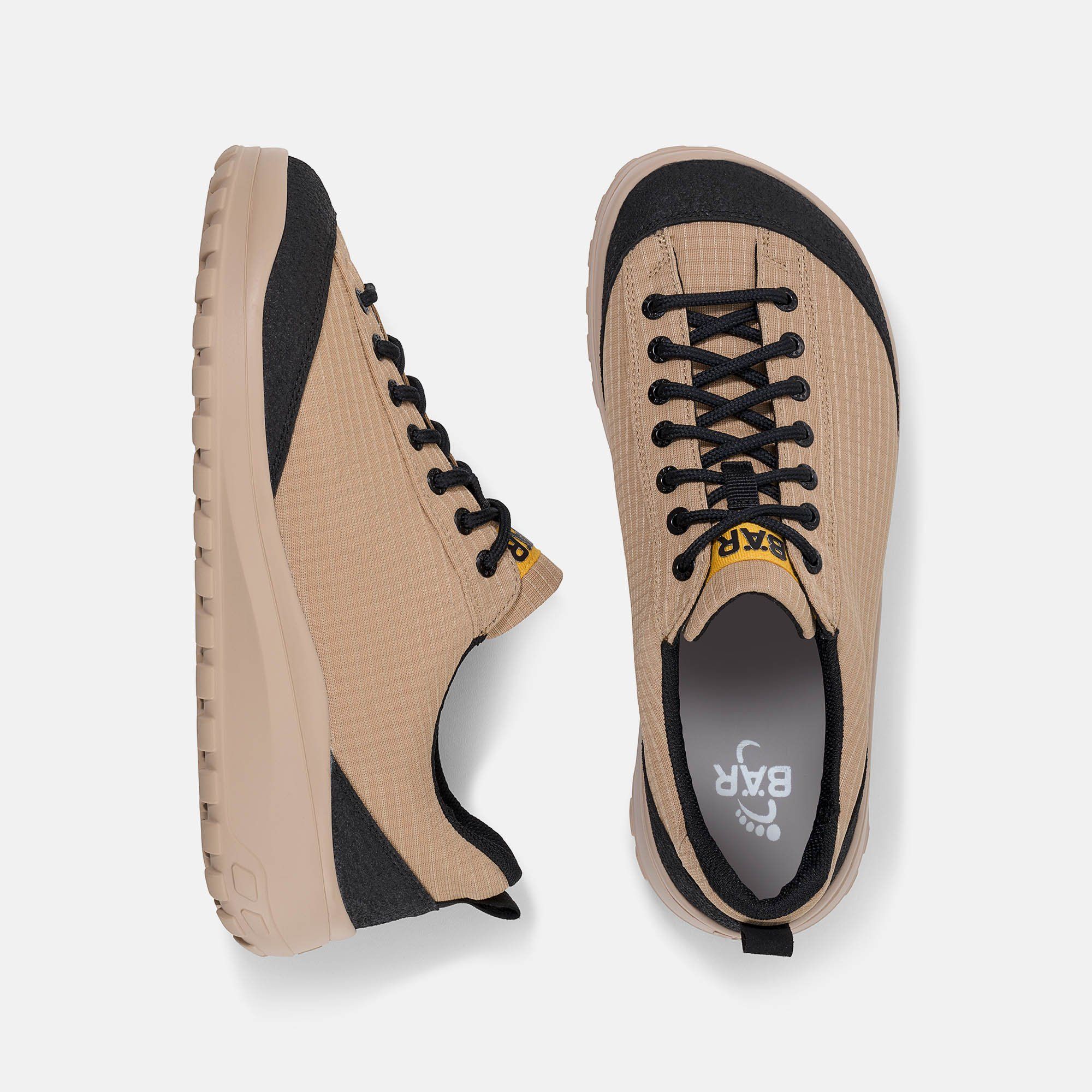 Ansicht von oben auf zwei beige Schnürschuhe mit schwarzem Rand und Schnürsenkeln. Gelbes Logo "BÄR".