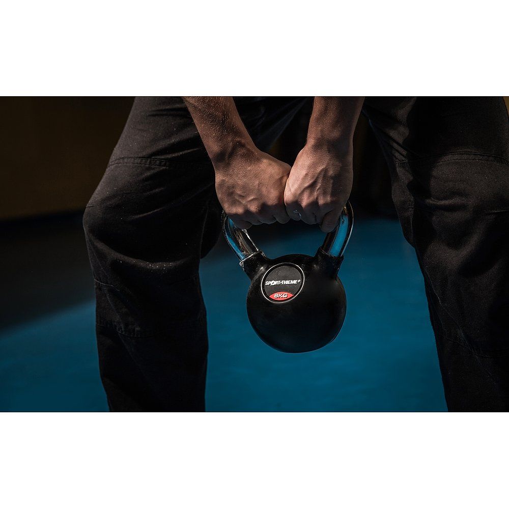 Person hält eine schwarze Kettlebell mit Chromgriff. Der Griff wird mit beiden Händen gehalten. Das Logo ist sichtbar.