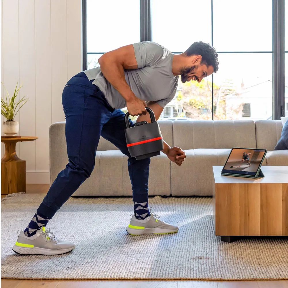 Homme s'entraînant avec une kettlebell. Haltère kettlebell noire avec bande rouge. Marque Bowflex.