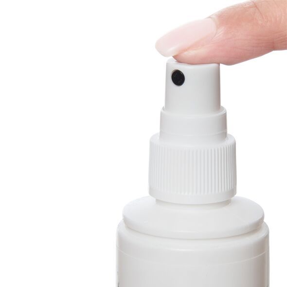 Nahaufnahme des Sprühkopfes einer weißen Flasche. Ein Finger drückt auf den Sprühkopf.