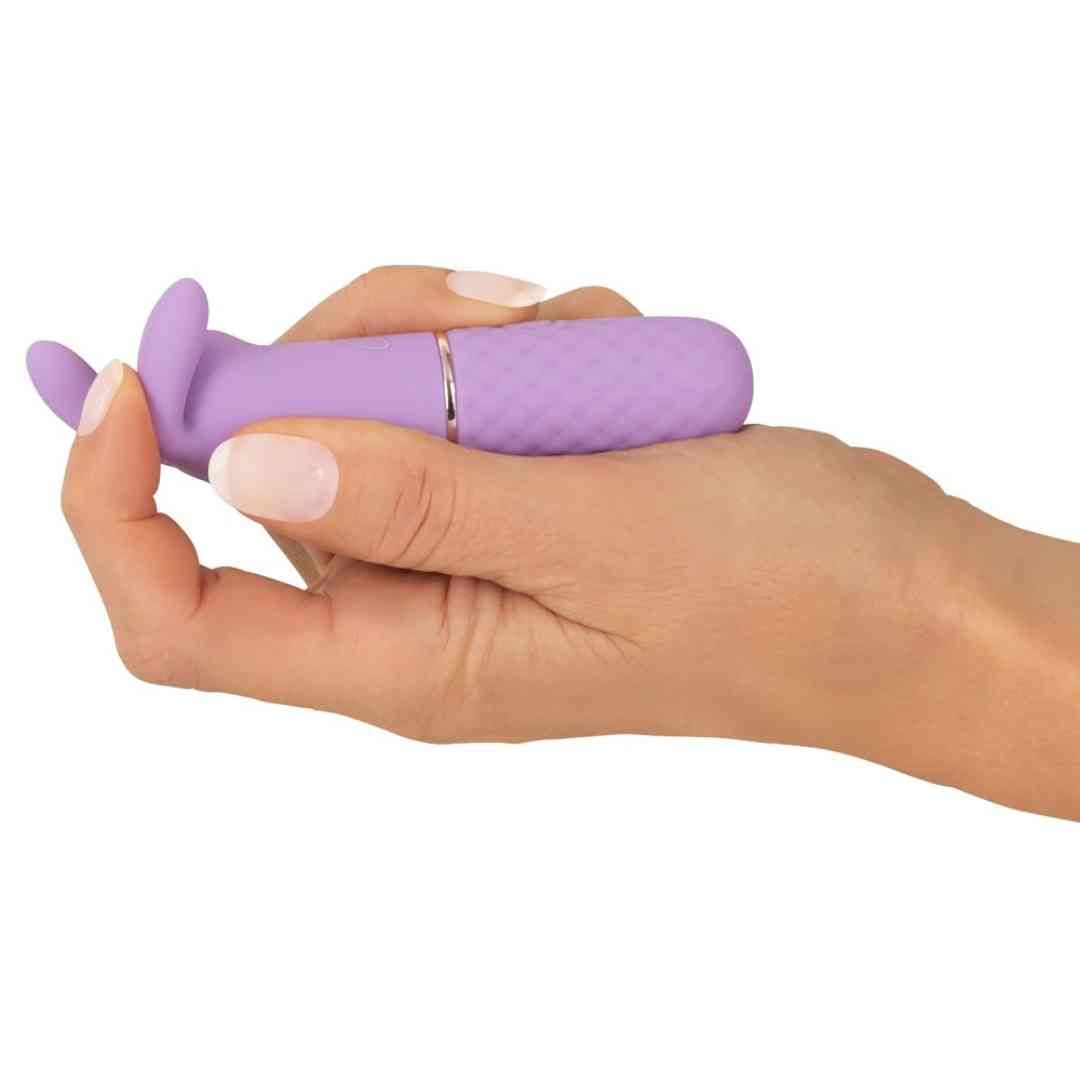 Lila Vibrator in Hand gehalten. Hasenohren-Design, geriffelte Basis, goldfarbener Ring.