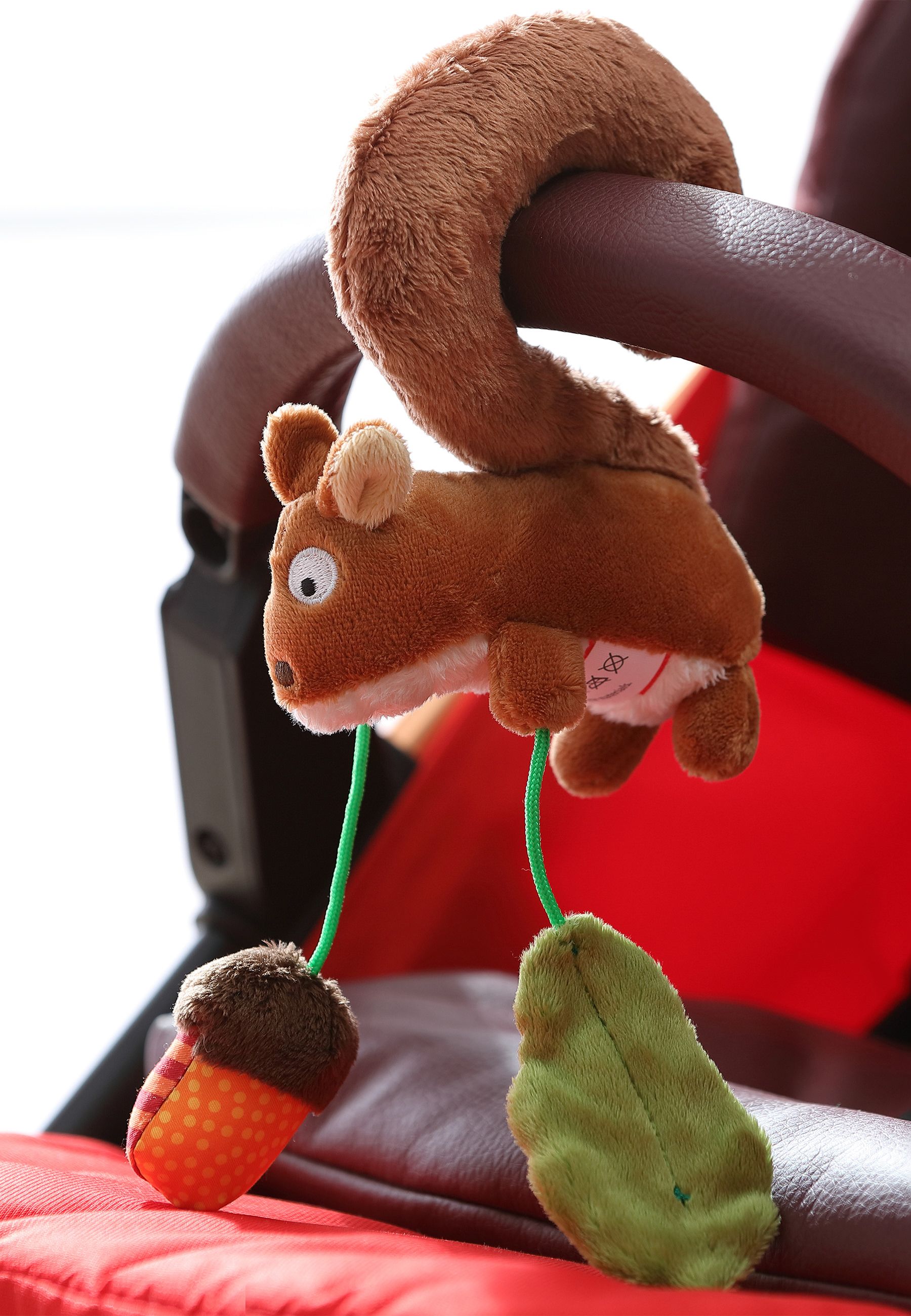 Plüsch-Eichhörnchen-Anhänger mit Eichel und Blatt, an Kinderwagengriff befestigt.