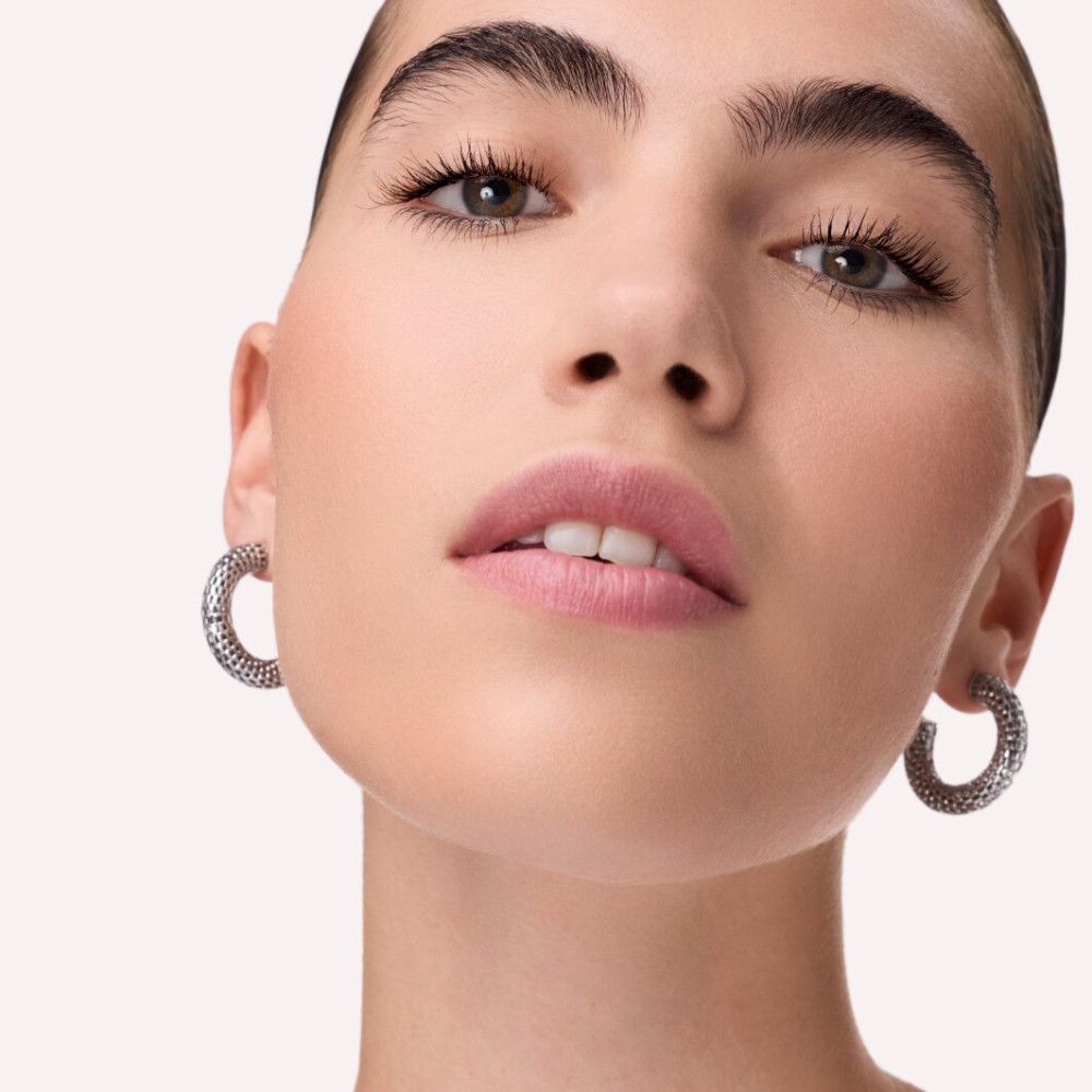 Nahaufnahme eines Gesichts mit silbernen Ohrringen. Die Person hat helle Haut und trägt Lippenstift.