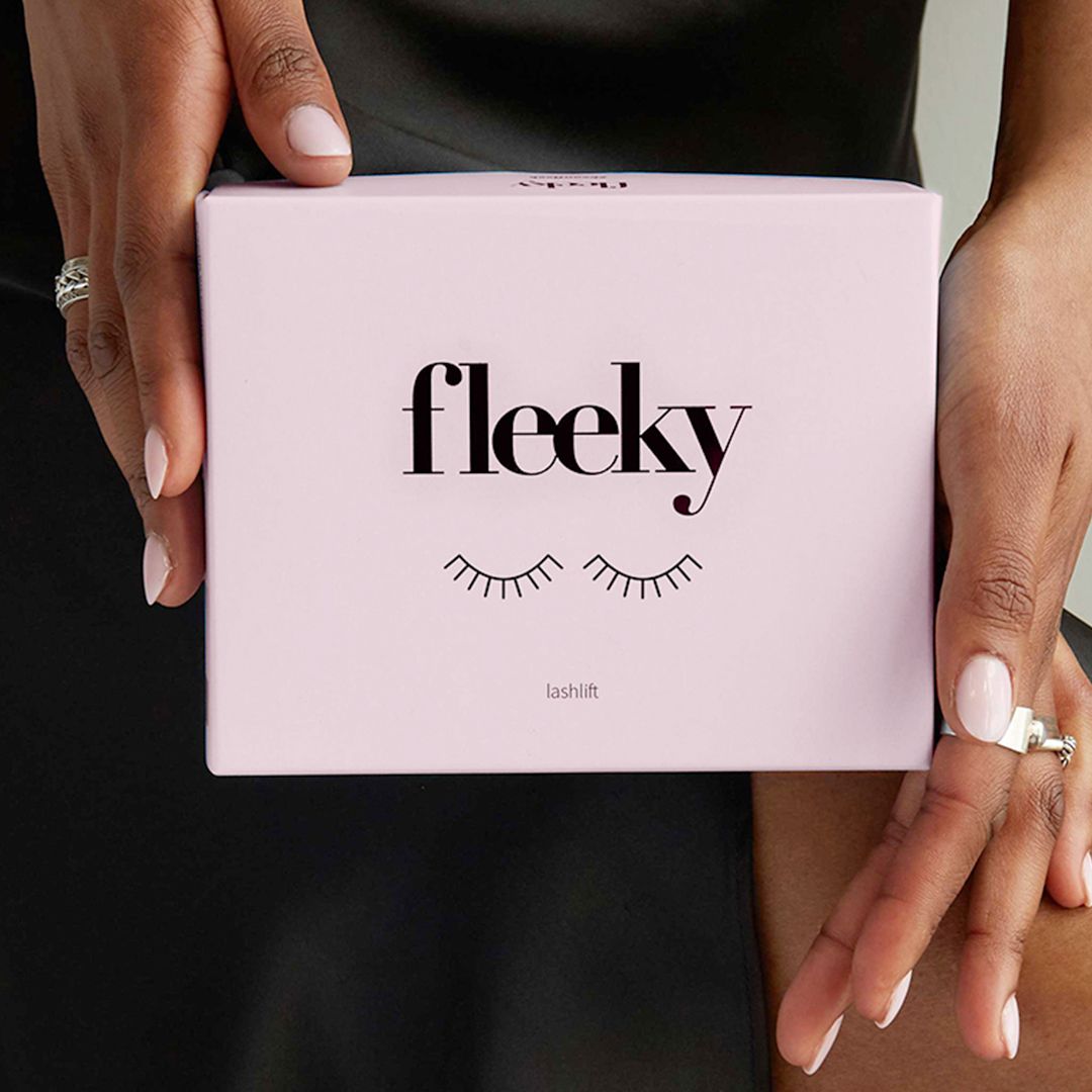 Rosa Box mit Aufdruck: fleeky, Lashlift. Gehalten von Händen mit lackierten Nägeln.