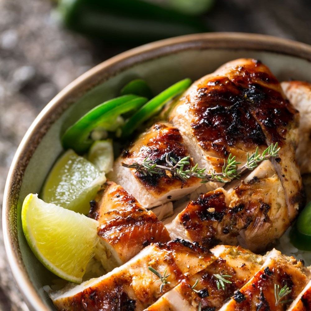 Gegrilltes Hähnchen mit Limetten und Jalapeños in einer Schüssel. Garniert mit Kräutern.