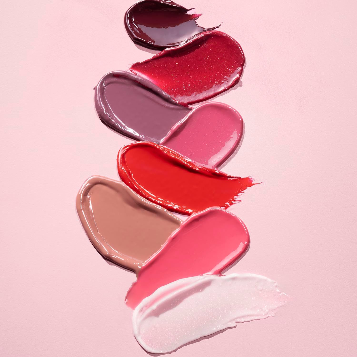 Verschiedene Lippenstiftfarben in Strichen auf rosa Untergrund. Farben: Dunkelrot, Rot, Rosa, Beige, Hellrosa, Weiß.