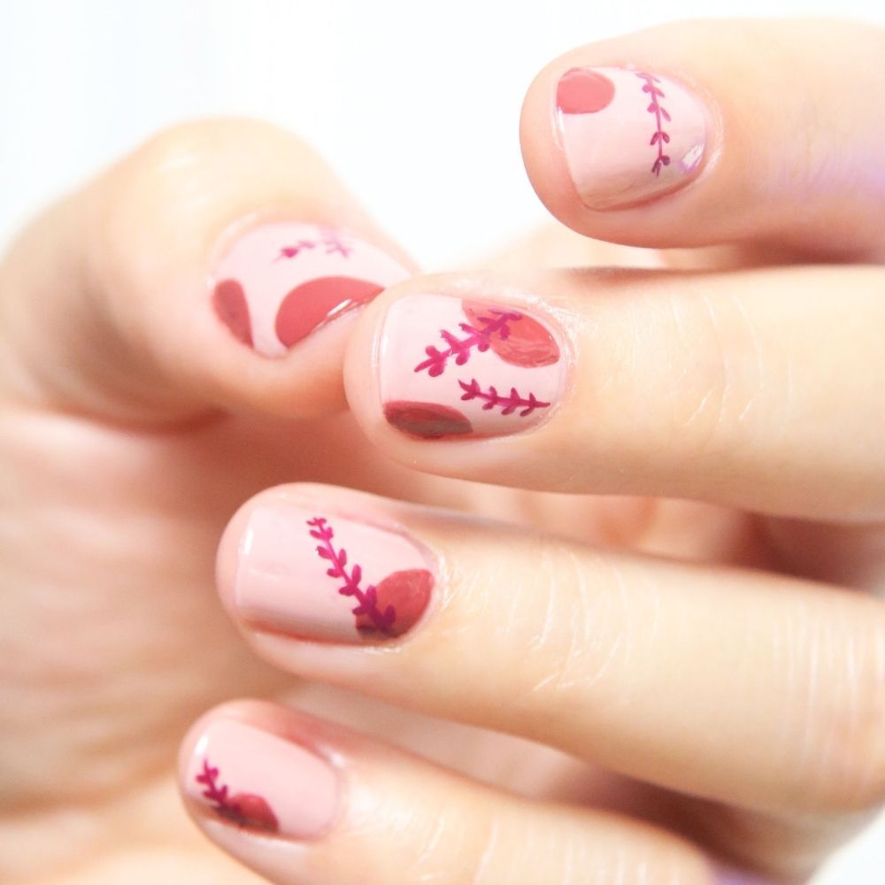 Nahaufnahme einer Hand mit rosa lackierten Nägeln. Rote Blätter- und Punktmuster auf den Nägeln.