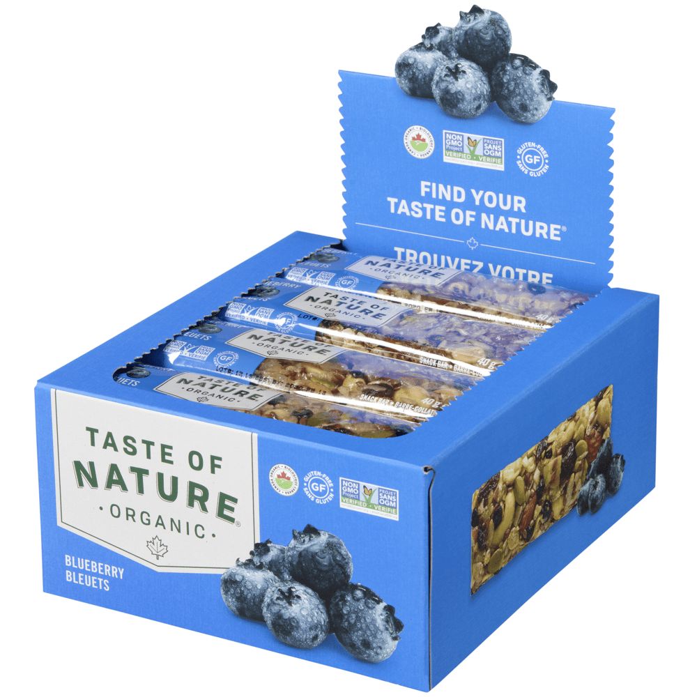 Eine blaue Kartonbox mit mehreren "Taste of Nature" Bio-Frucht- und Nussriegeln mit Blaubeeren. Die Box zeigt das Markenlogo und den Hinweis "Blaubeere". Obenauf sind Blaubeeren abgebildet. Die Box enthält mehrere einzeln verpackte Riegel.