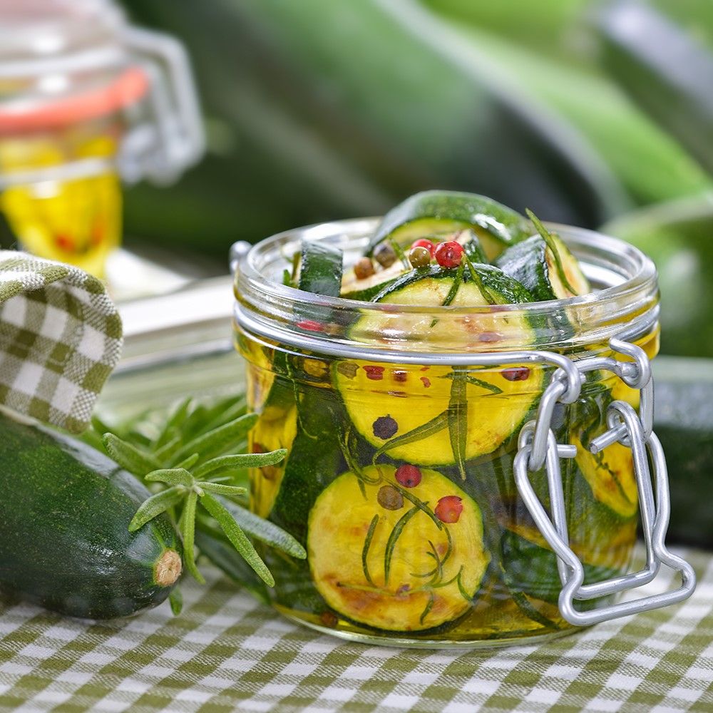 Glas mit eingelegten Zucchinischeiben, Rosmarin und Pfefferkörnern. Auf grün-weiß kariertem Tuch.