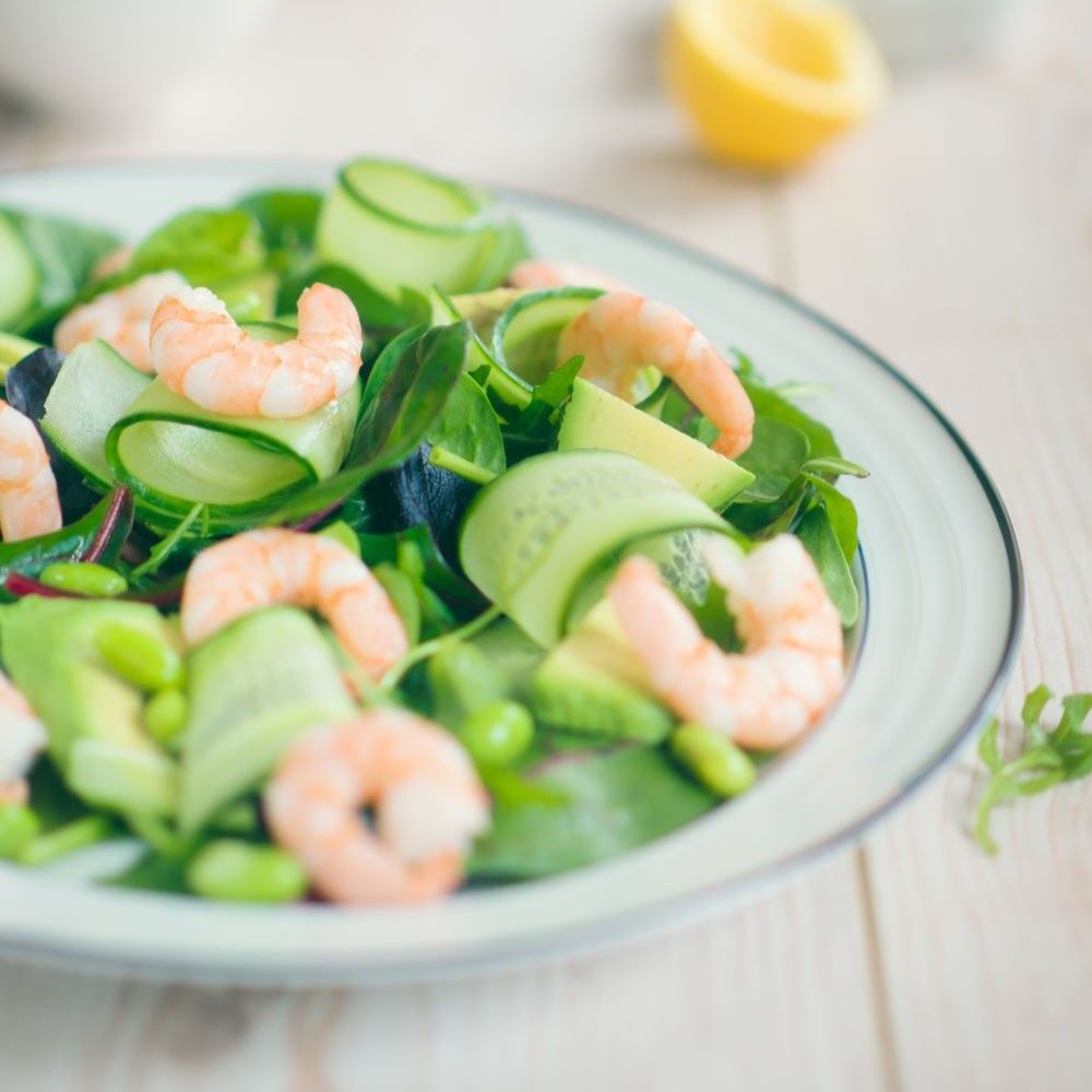 Salatteller mit Garnelen, Gurken, Avocado und Edamame. Helle Holzoberfläche.