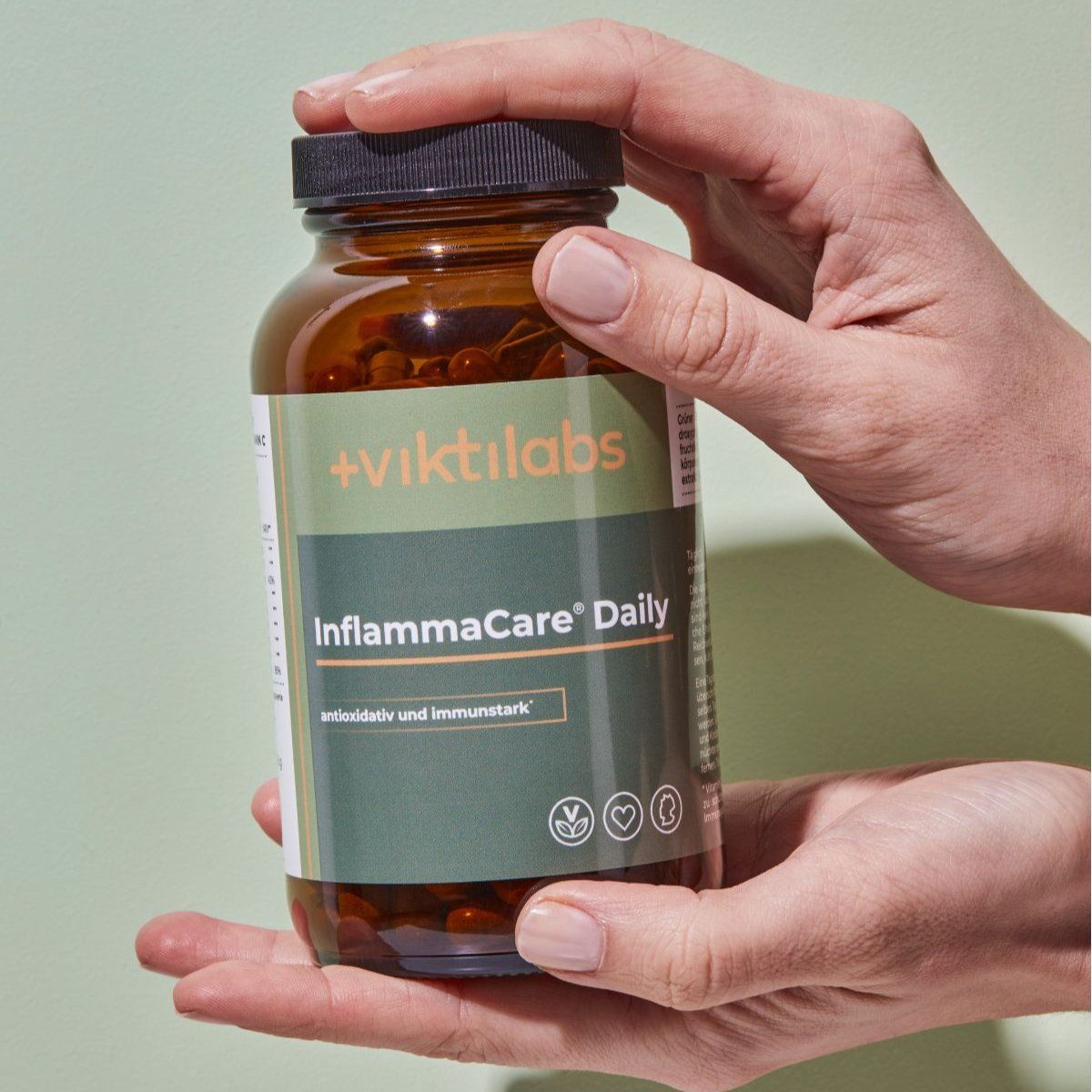 Hände halten eine braune Glasflasche mit schwarzem Deckel und grünem Etikett. Aufschrift: Viktilabs InflammaCare® Daily.