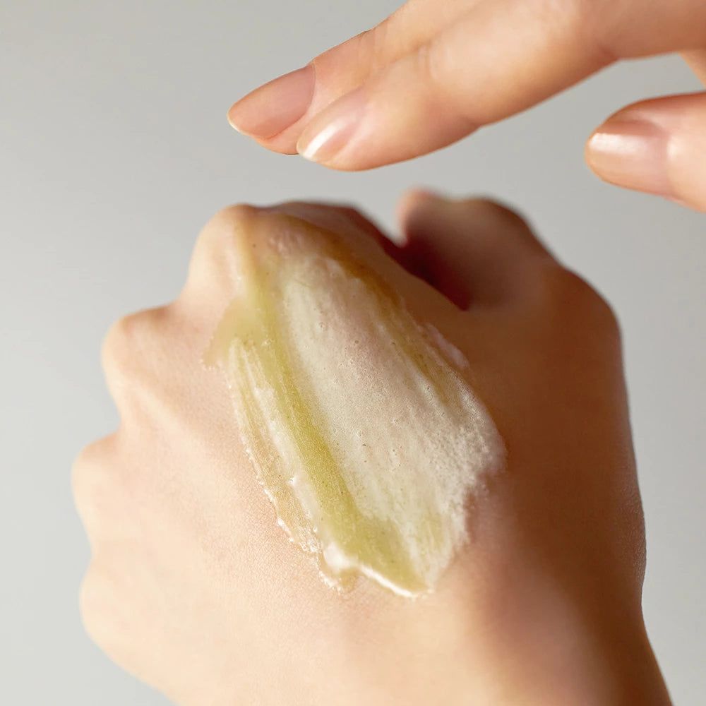 Hand mit gelblicher Substanz. Ein Finger berührt die Substanz. Keine weitere Produktinformationen sichtbar.