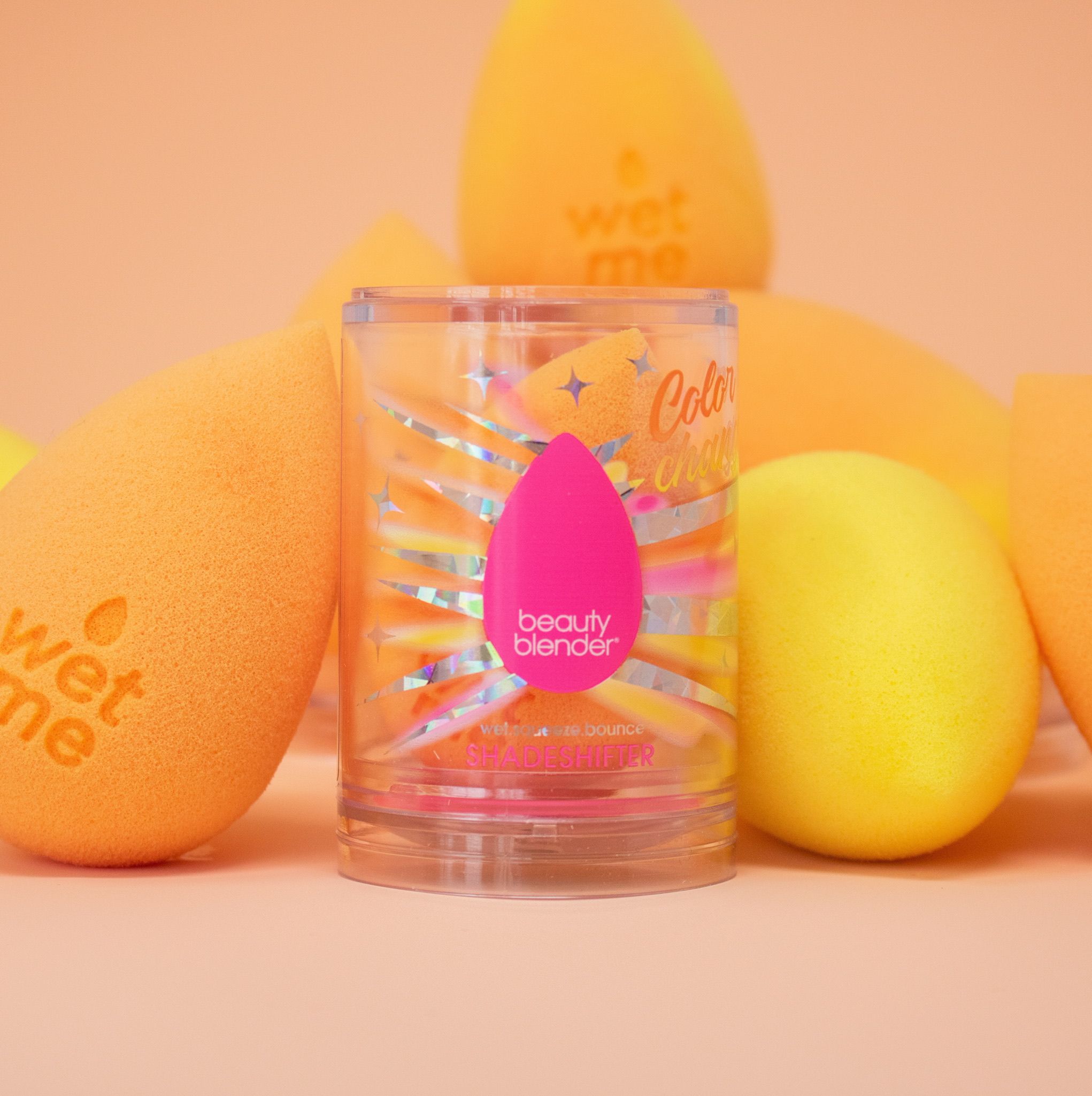 Beautyblender Make-up-Schwamm im Behälter, umgeben von orangen und gelben Schwämmen.