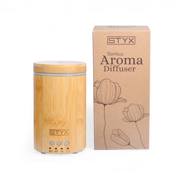 Aroma Diffusor aus Bambus mit STYX-Logo und Bedienknöpfen. Neben einer braunen Verpackung mit floralen Illustrationen und Produktbezeichnung.