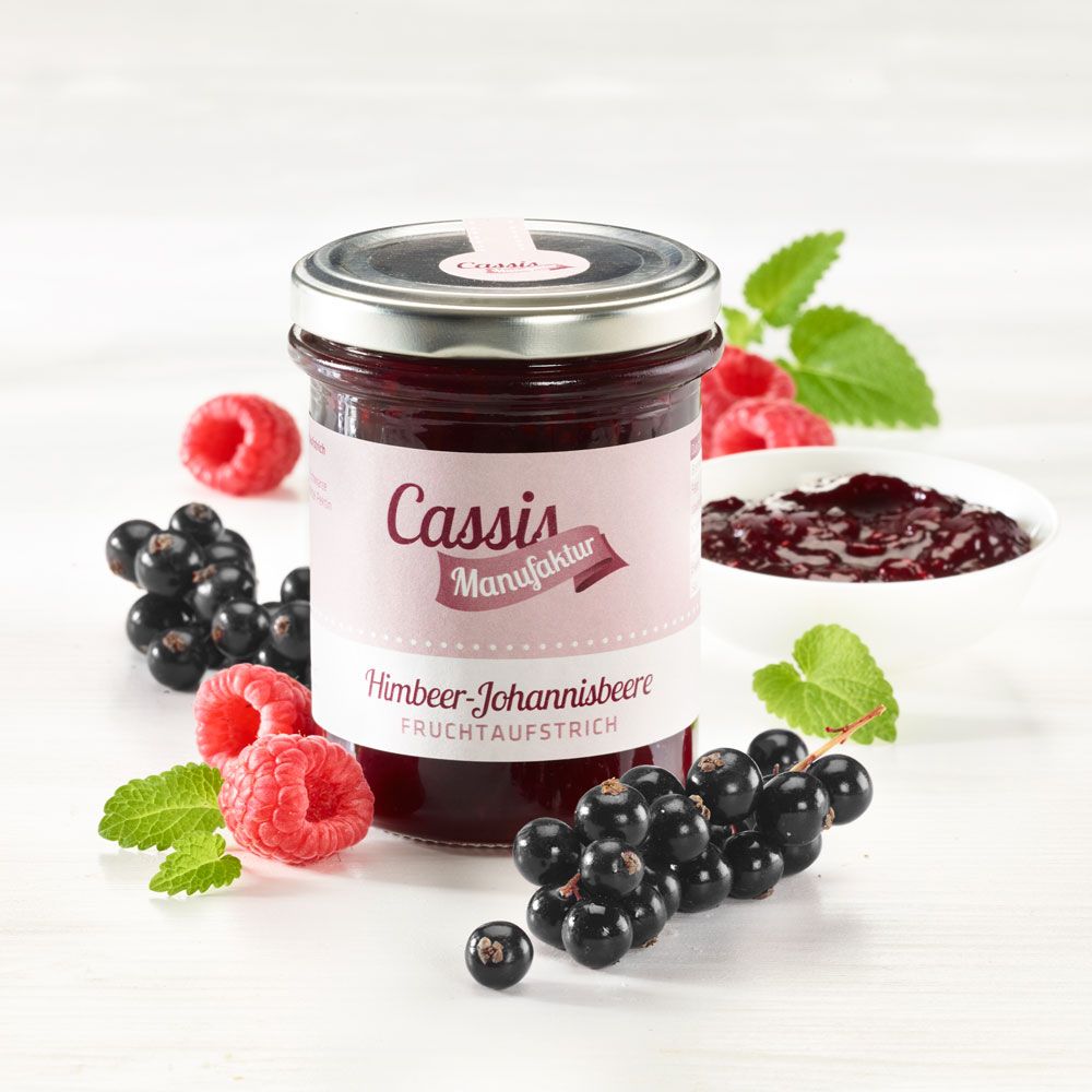 Glas Fruchtaufstrich Himbeer-Johannisbeere, umgeben von Früchten und Blättern. Etikett "Cassis Manufaktur".