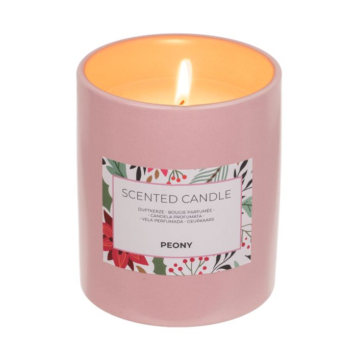 Roze geurkaars met etiket. Opschrift: Scented Candle, Peony. Kaars brandt. Meertalige productaanduidingen.